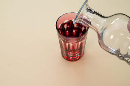 A closeup shot of a bottle of water pouring on a glass isolated on a pink surface with copyspaceの写真素材