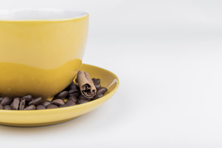 coffee composition, close-up of part of a yellow ceramic cup with its plate full of coffee beans and a piece of cinnamon stick, with space to writeの写真素材