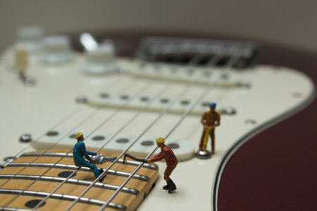A closeup shot of small figures of working people on an electric guitar