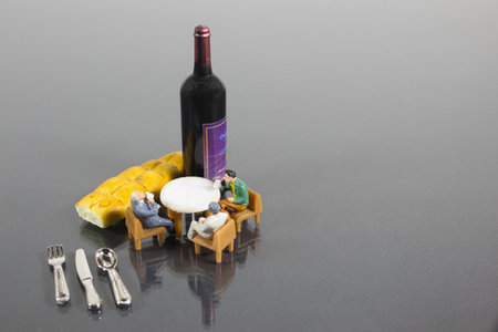 A shot of a wine bottle and mini figures of peoplÐµ sitting around tableの写真素材