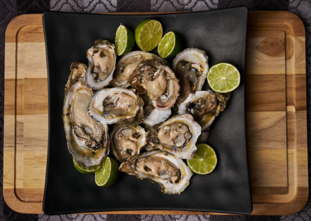 A top view of fresh oysters with lime slices on a wooden board