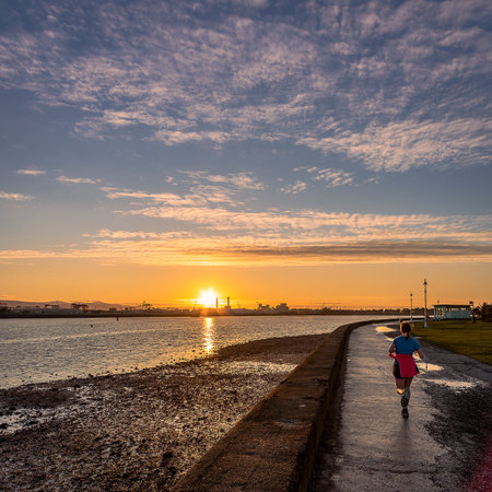 A back view of a female running on the coast of Dublin harbor at sunsetの写真素材