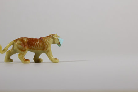 A closeup of a plastic lioness toy wearing a protective facemask on a gray backgroundの写真素材