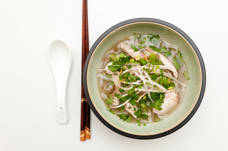 A top view of Vietnamese pho soup with a spoon and Chinese wooden sticks isolated on a white surface