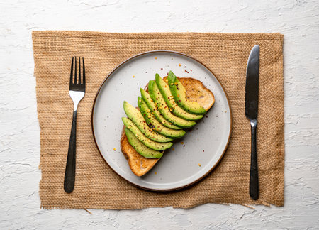 A top view of a delicious avocado toast on a white plate, with fork and knifeの写真素材