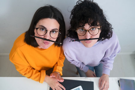 A view of two friends having fun with pencils as mustaches dressed in hoodiesの写真素材