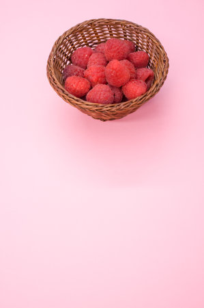 A vertical shot of fresh raspberries in a basket isolated on pink background