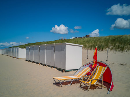 A couple of yellow sunloungers with white stripes on a sandy beach with cabinsの写真素材