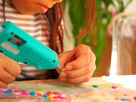 A little girl doing a manual and artistic activity with a glue gunの写真素材