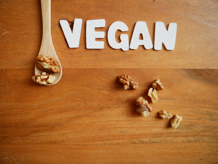 The word "VEGAN" in white letters with walnut kernels and a spoon on a wooden backgroundの写真素材