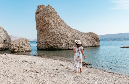 Woman in elegant long white summer dress standing on beautiful Beritnica beach with large rock formations on Pag island in Croatia.の写真素材