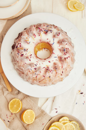A vertical shot of a delicious citron cake with glaze and flower on top on a white tableの写真素材