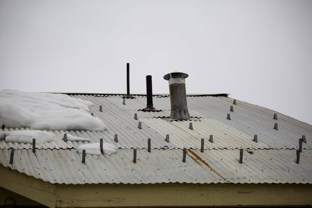 A shot of the roof with a chimney and snow covering one portion of the surface.の写真素材