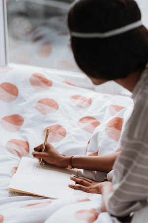 An African female writing notes in a diary while sitting on the bedの写真素材