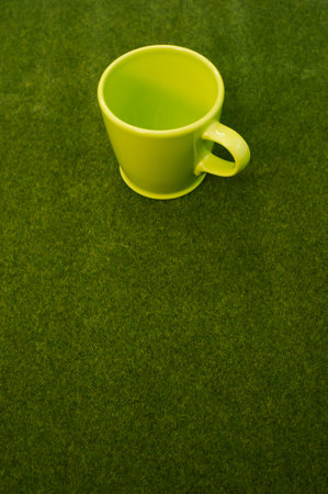 A vertical shot of a green cup on the grass with a copy space