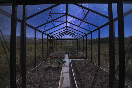 A beautiful shot of a glass greenhouse in the middle of a field on background of the starry skyの写真素材