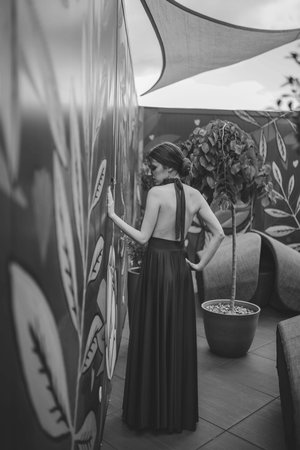 A grayscale shot of a young elegant woman wearing a long dress in an outdoor cafeの写真素材