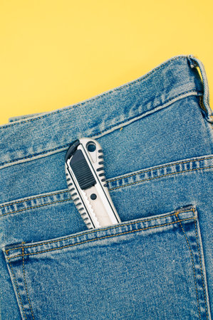 A vertical shot of a pocket knife in the jeans pocket on a yellow backgroundの写真素材