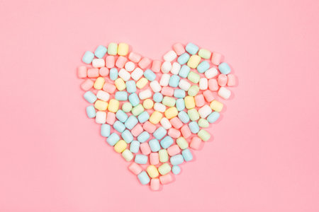A top view of colorful sweet candies in the form of a heart on pink background