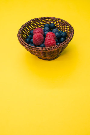 A closeup shot of blueberries and raspberries in a basket on a yellow backgroundの写真素材