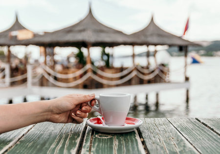 A person grabbing a cup of coffee on a wooden table at the beachの写真素材