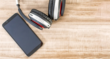 A top view of a cell phone and wireless headphones on a wooden table