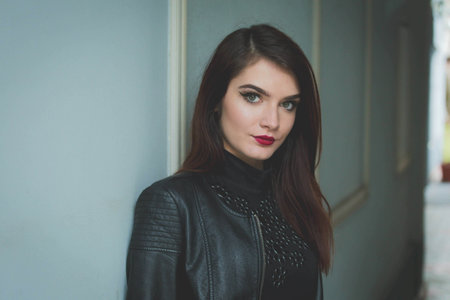 A beautiful Caucasian female with red lipstick and leather jacket posing outdoorsの写真素材