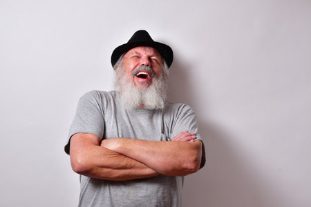 An old male with a grey shirt and black fedora hat having a good laughの写真素材