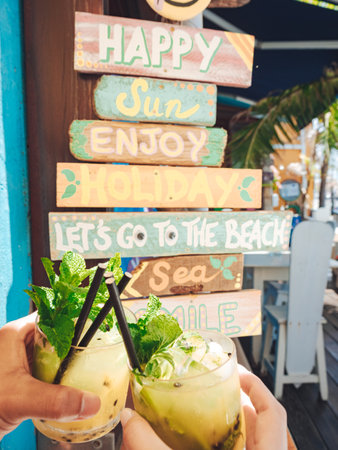 A closeup shot of a couple's hands toasting their cocktails against wooden quote poster backgroundの写真素材