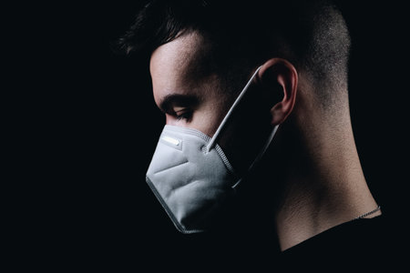 A side view of a young caucasian male in a protective face mask on a black backgroundの写真素材