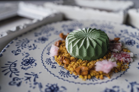 A closeup of a small green cake on biscuit crumbles with nuts and sugar on a plate on the tableの写真素材