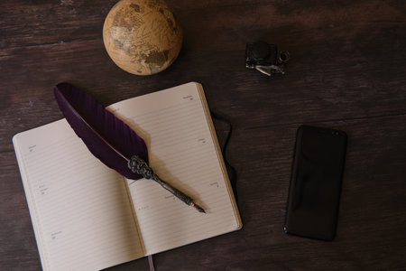 A top view shot of a globe, notebook, inkwell, pen, and a cellphone on the wooden table