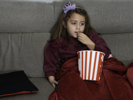 A Latina girl eating popcorn and watching a movie with light offの写真素材