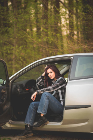 A young dark-haired Caucasian female in a checkered shirt posing in a car