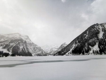Frozen lake in front of snowy mountains in the Alps; cloudy sky; winter wonderland Austriaの写真素材