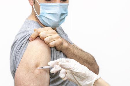 A male with a face mask receiving Covid19 vaccinationの写真素材