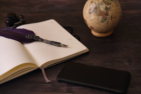 A closeup shot of a globe, notebook, inkwell, pen, and a cellphone on the wooden tableの写真素材