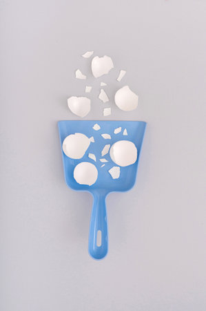 A vertical shot of chicken eggshells in a blue plastic scoop on a white surface