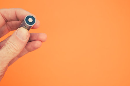 A closeup shot of a hand holding a battery on a light orange backgroundの写真素材