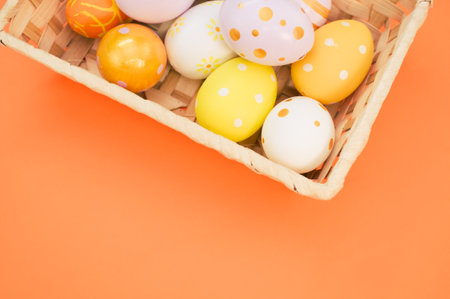 A woven basket filled with colorful Easter eggs on orange background