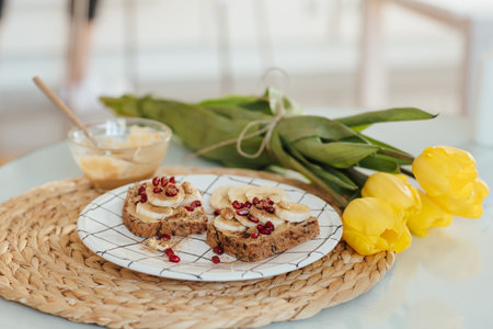 A shot of the peanut butter toast with banana slices and pomegranate on a plate decorated with...