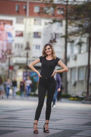 A vertical shot of a young blonde female in black pants, blouse and high heels posing in the street