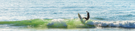 A panoramic shot of a person surfing on the waves