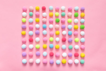 A top view of colorful pom pom balls forming a square shape on pink background