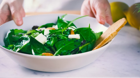 A selective focus of a bowl of fresh spinach salad with blurred person's hands holding itの写真素材