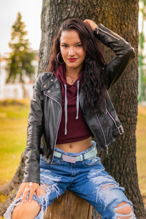 A vertical shot of a beautiful Latin female in the city park next to a tree