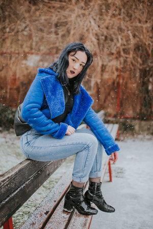 A young Caucasian female with black hair wearing a black shirt and a blue coat posing outdoorsの写真素材