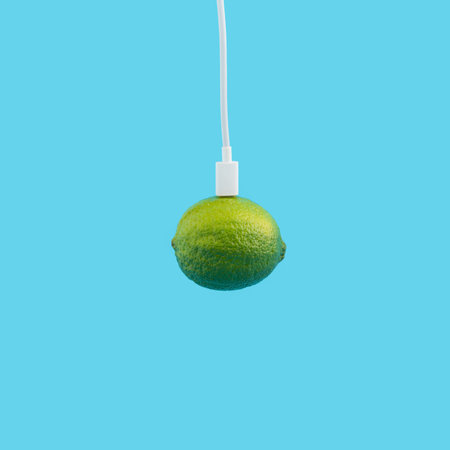 A white phone charger attached to a lime isolated on a blue background