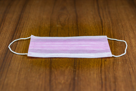 A selective focus shot of a pink surgical cotton mask on a wooden surface