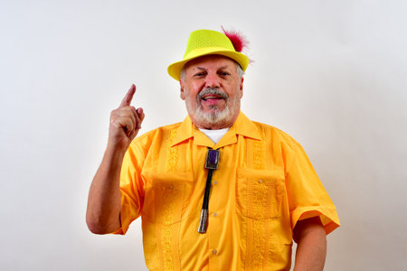 A senior male in a cute yellow outfit holding up one finger front of a white wallの写真素材
